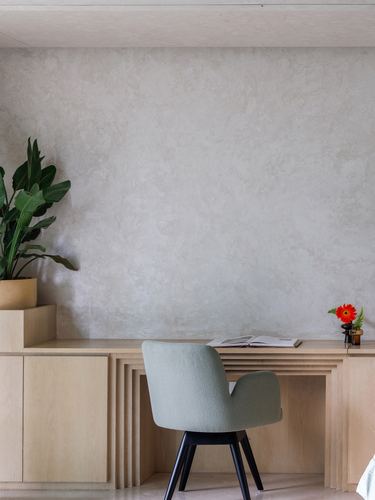 Built-in wood desk against textured plaster wall with green boucle chair and potted plant