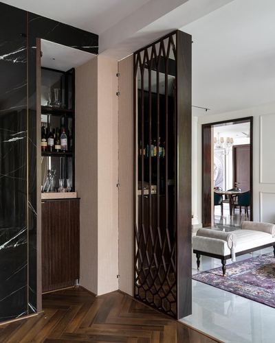 Hallway with black marble wall, wood-framed lattice door opening to a hidden bar nook, living room beyond