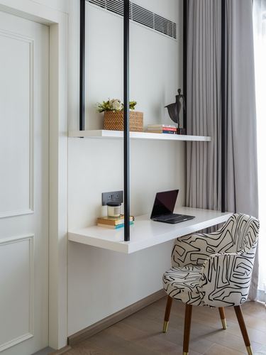 Wall-mounted desk with laptop, shelf above, and patterned chair by curtained window