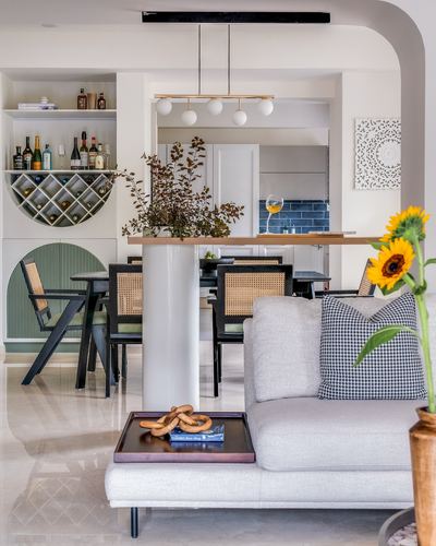 Open living-dining space with cane chairs, arched wine niche, sunflowers, and glass pendant lighting in Bangalore home