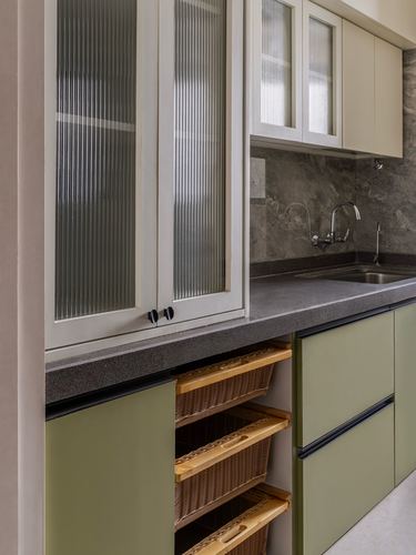 Sage green kitchen cabinetry with reeded glass uppers and woven basket drawers