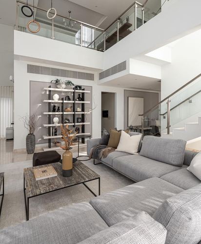 Grey sectional sofa and stone-topped coffee table in a double-height living room with staircase and mezzanine.