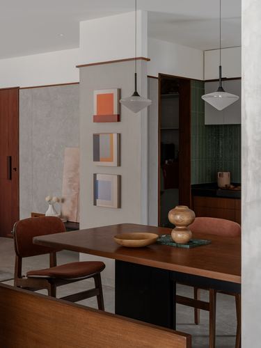 Dining table with pendant lights, framed art on column, green tiled kitchen beyond
