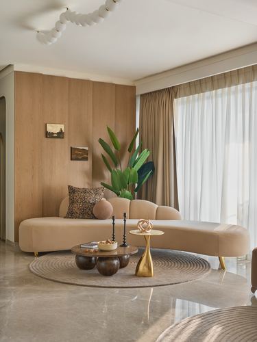 Curved beige sofa against wood-paneled wall with round rug and sculptural coffee tables