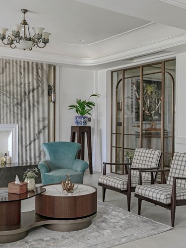 Living room with teal armchair, checkered chairs, marble accent wall and brass-framed glass cabinet