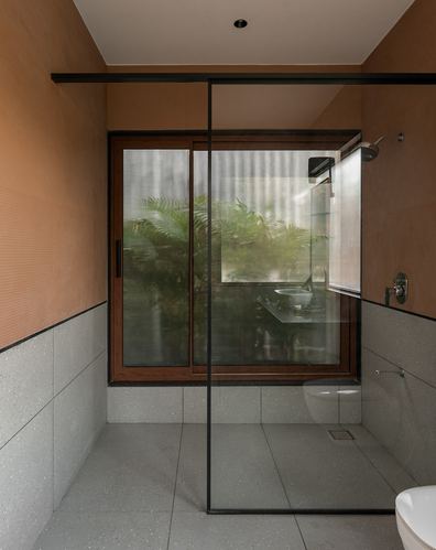Bathroom with terrazzo tile, terracotta plaster wall, and glass shower facing a green window view