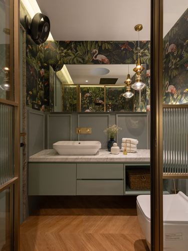 Bathroom vanity with flamingo wallpaper, sage cabinetry, marble-look counter, brass pendant lights, herringbone wood floor