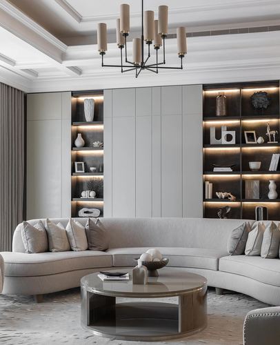 Greige living room with curved sofa, round stone coffee table, and lit display shelving under a coffered ceiling