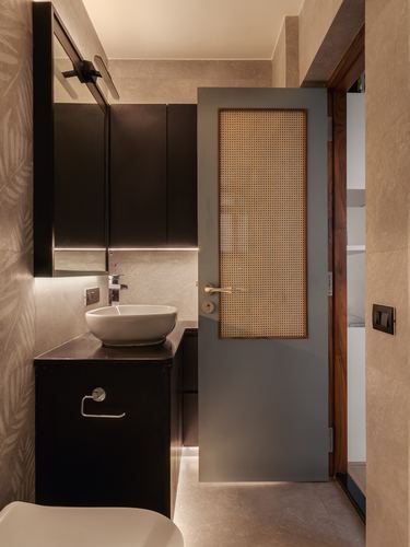 Dark bathroom vanity with vessel sink beside a cane-paneled door leading to a walk-in closet