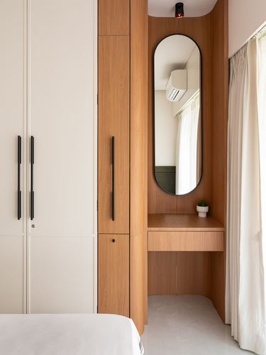 Wooden dressing nook with oval mirror beside beige wardrobe in minimal bedroom