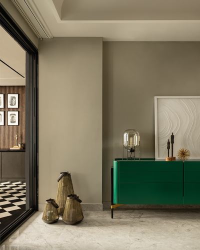 Green lacquered sideboard with lamp and art against a taupe wall beside a doorway with cane baskets