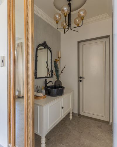 Powder room vanity with black vessel sink, carved mirror, and brass chandelier beside a mirrored door