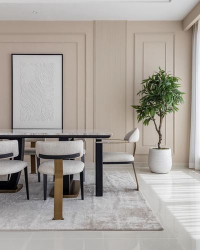 Beige dining room with marble table, cream chairs, framed art, and a large potted plant