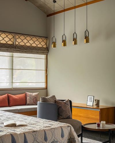 Bedroom corner with window seat, patterned blinds, and four brass pendant lights hanging from a high ceiling