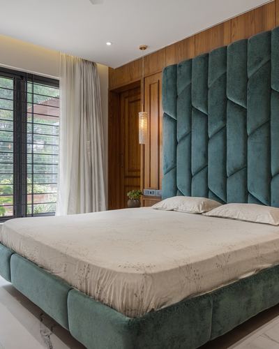 Bedroom with teal channel-tufted headboard, wood-panelled wall, pendant light, and sheer curtains by a window.