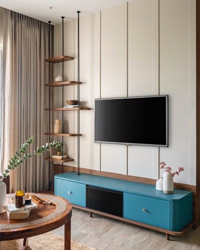 Living room with teal TV console, teak suspended shelves, and paneled cream wall