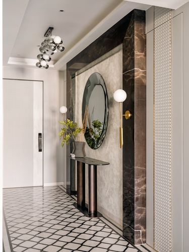 Marble-clad foyer wall with round mirror, brass sconce, and geometric floor tiles