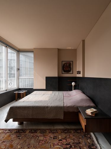 Bedroom with terracotta walls, dark ribbed lower wall, low wood bed and city view window
