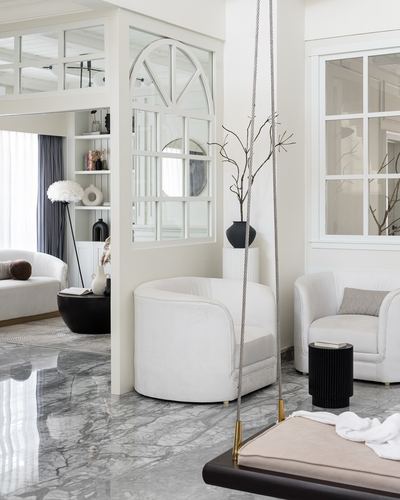 White living room with arched mirror, curved white armchairs, and a hanging swing over marble floor