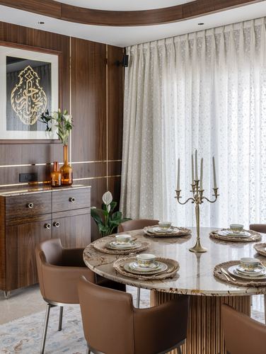 Round marble-look dining table set with brass candelabra beneath a curved wood ceiling