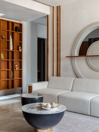 Living room corner with boucle sofa, round black coffee tables, wooden shelving, and carved circular wall mirror
