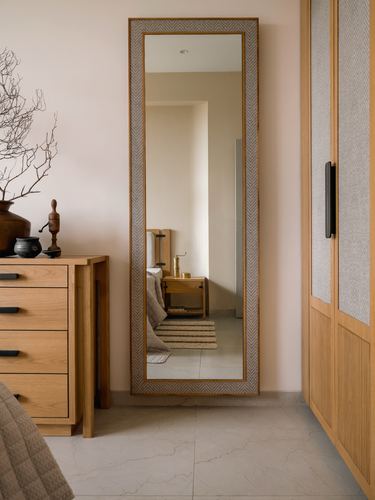Bedroom corner with tall framed mirror, wooden chest of drawers, and cane-detailed wardrobe