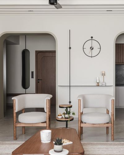 Two bouclé and wood armchairs flank a round side table beneath a wall clock in an arched living room
