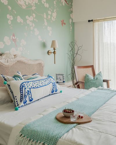 Bedroom with mint floral wallpaper, cane headboard, blue horse pillow, and breakfast tray on bed