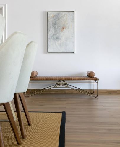 Dining nook with cream chairs, wood floor, leather bolster bench, and abstract framed art above