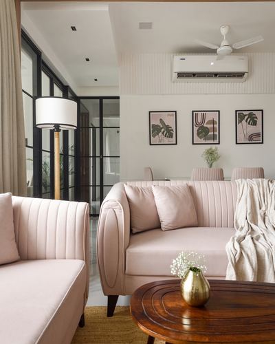 Blush pink ribbed sofas around round wood coffee table with brass vase and botanical wall art