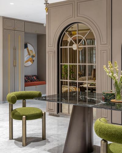 Dining area with green boucle chairs, marble table, and arched mirrored doorway in a Mumbai apartment