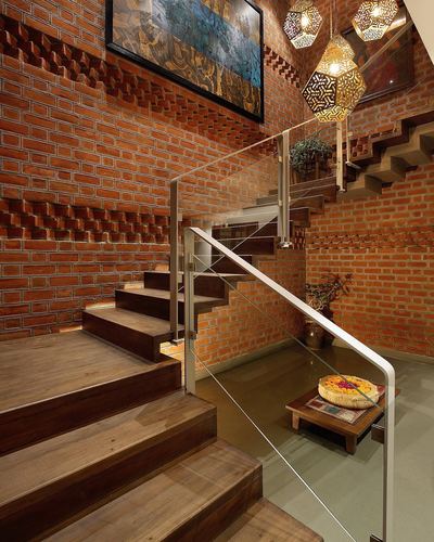 Wooden staircase with glass railing against a textured exposed brick stairwell wall, lit by moroccan-style pendant lanterns