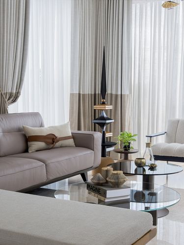 Living room vignette with taupe leather sofa, glass coffee tables, and sheer floor-to-ceiling curtains
