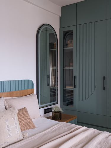 Bedroom corner with green fluted wardrobes, arched mirror, and upholstered headboard bed