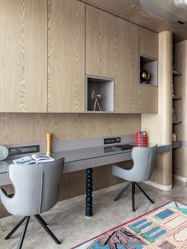 Home study nook with wood-paneled wall, glass-top desk, and two grey swivel chairs