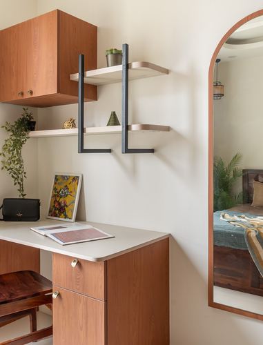 Wooden study nook with black metal shelving and arched mirrored doorway into bedroom