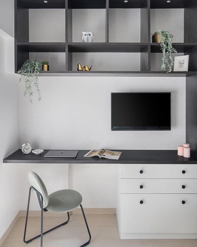 Minimalist home study nook with black shelving, mounted TV, white cabinetry and a green chair