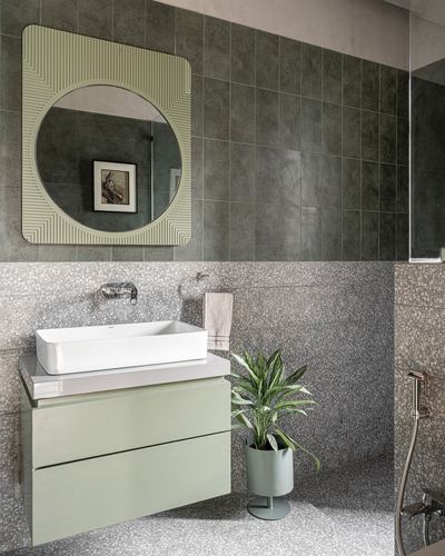 Bathroom with round ribbed mirror, terrazzo counter and sage green vanity below grey tiled wall