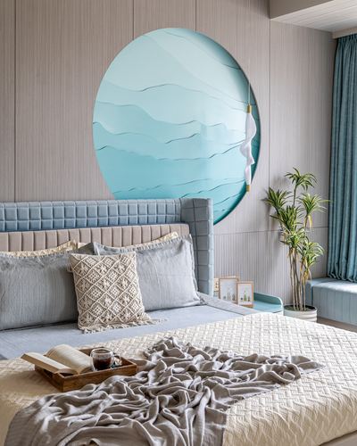 Bedroom with tufted blue headboard, layered pillows, and a large circular blue wave-patterned wall art