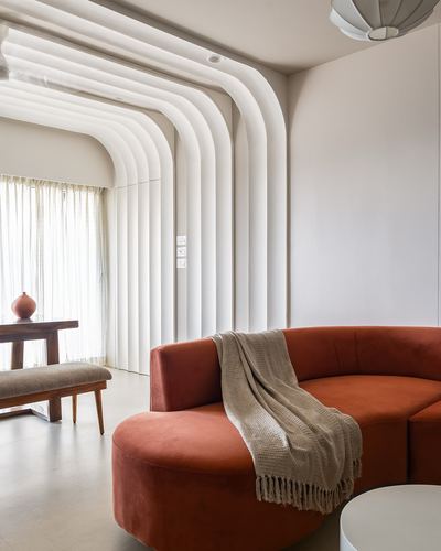 Curved terracotta sofa beneath ribbed white archway ceiling in a minimalist living room