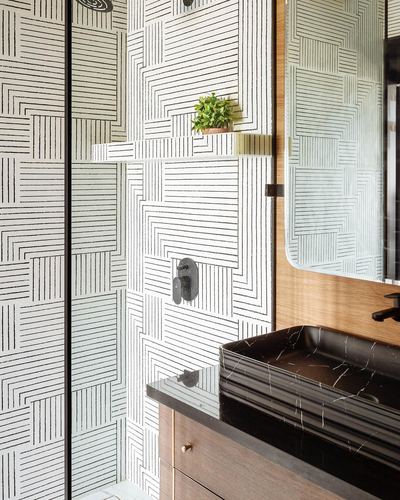 Bathroom with black-and-white geometric tiled shower wall, wood vanity, and black marble vessel sink