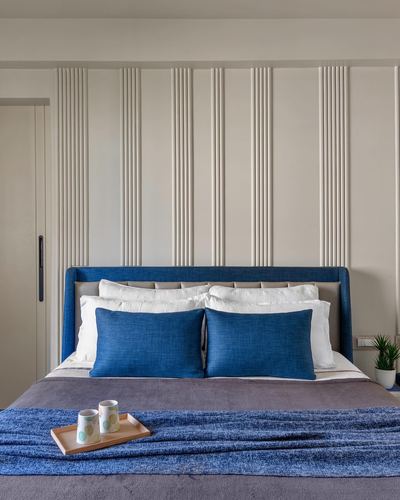 Bed with blue upholstered headboard against a fluted off-white panelled wall.