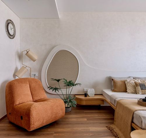 Orange boucle chair beside curved plaster wall with arched niche and bed in warm bedroom