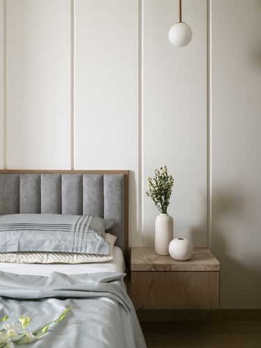 Grey channel-tufted headboard beside floating wood nightstand with stone top and globe pendant light