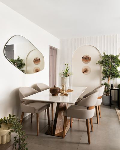 Dining room with marble table, beige upholstered chairs, arched wall niche and organic mirror