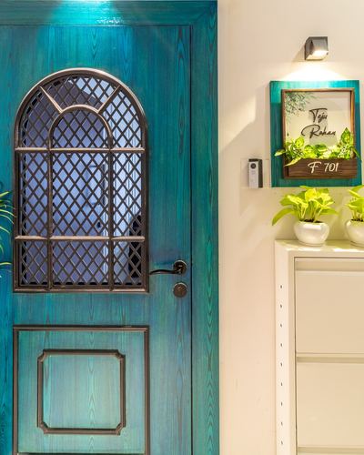 Teal stained wooden door with arched grille window beside white entry console and plants