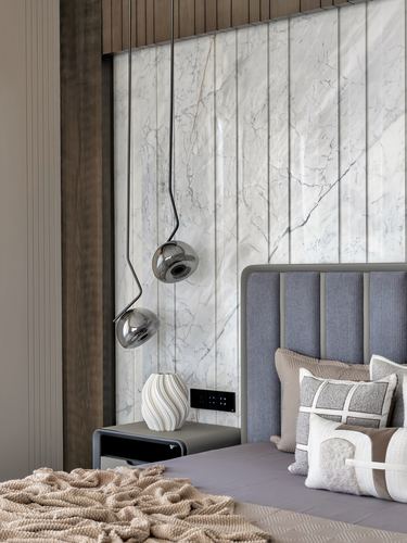 Bedroom corner with marble wall, chrome pendant lights, upholstered headboard and layered cushions