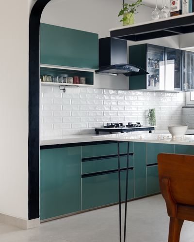 Teal cabinetry kitchen with white brick-look backsplash and black chimney hood, seen through a black arch