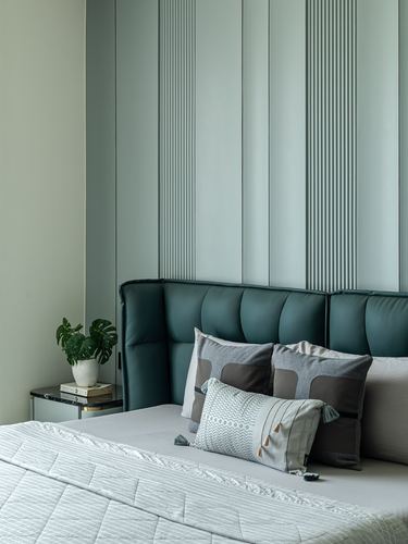 Bed with teal tufted headboard against fluted sage green wall panelling, plant on side table