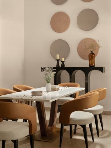 Dining room with white stone table, orange velvet chairs, and circular wall art above black console